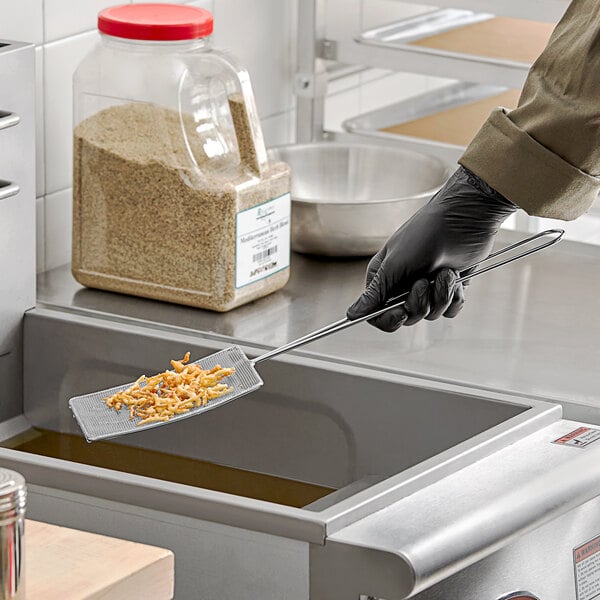 A person in a black glove using a Choice rectangular fine mesh skimmer to stir something in a professional kitchen.