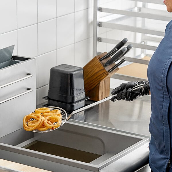 A woman in a blue uniform using a Choice 7" Round Spiral Skimmer to remove food from a deep fryer.