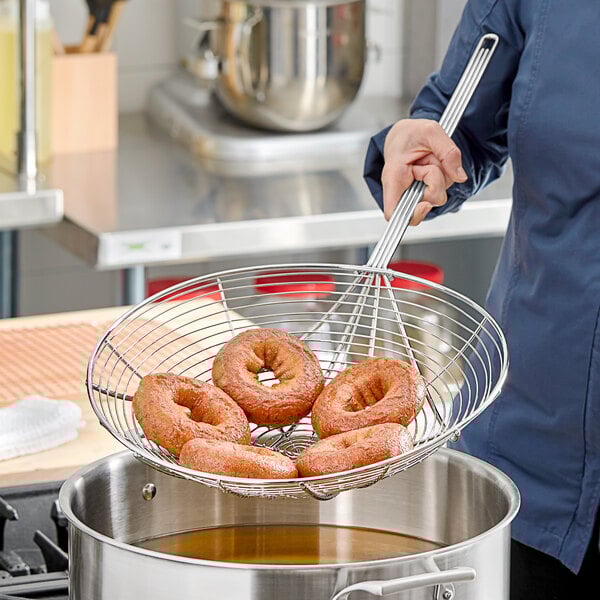 A woman using a Choice 14" Spiral Skimmer to hold a doughnut over a pot.