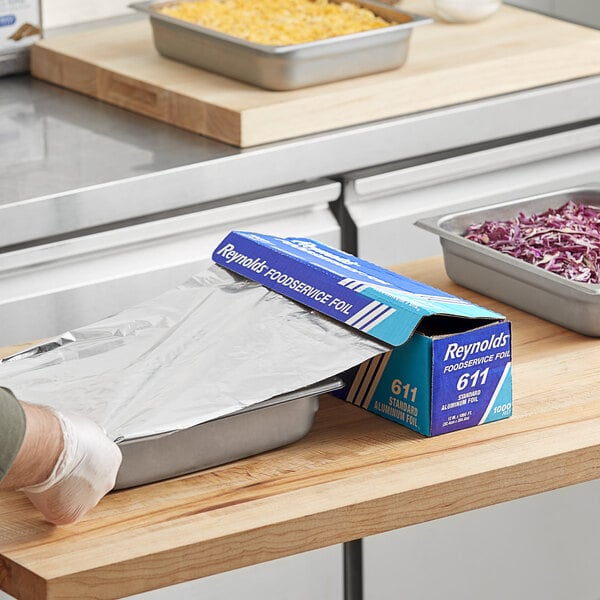 A person using Reynolds aluminum foil to cover a food container.