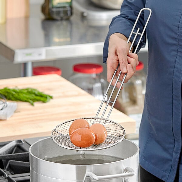 A person using a Choice round wire skimmer to lift eggs from a pot.