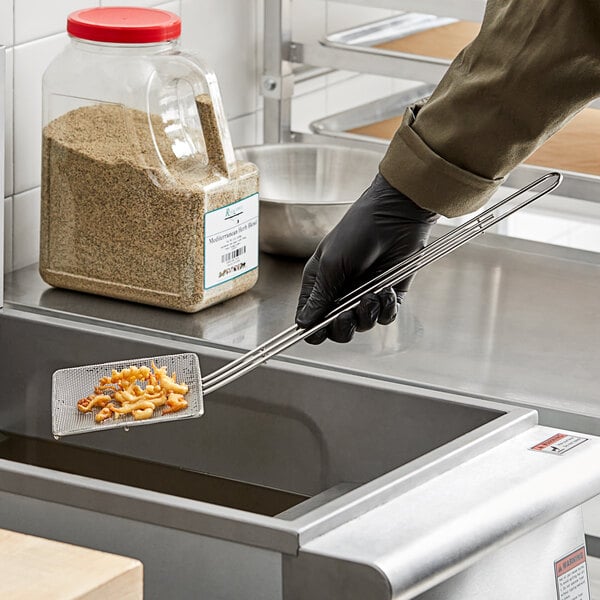 A person in black gloves using a Choice square fine mesh skimmer over a bowl of food.