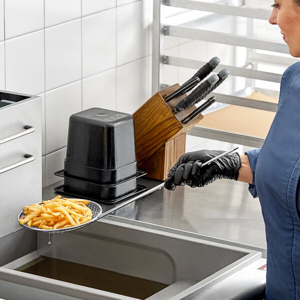 A woman in a blue uniform using a Choice 7" Round Coarse Mesh Reinforced Skimmer to hold a tray of french fries.