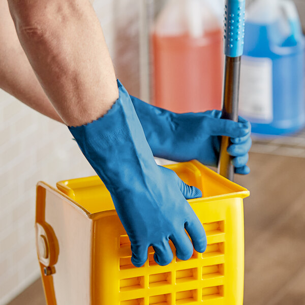 A person wearing Cordova blue latex rubber gloves cleaning a bucket with a mop.