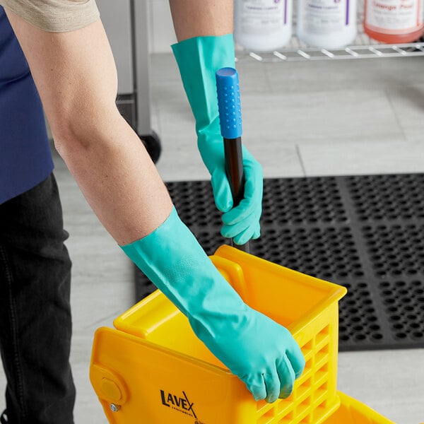 A person wearing Cordova green gloves using a yellow container.