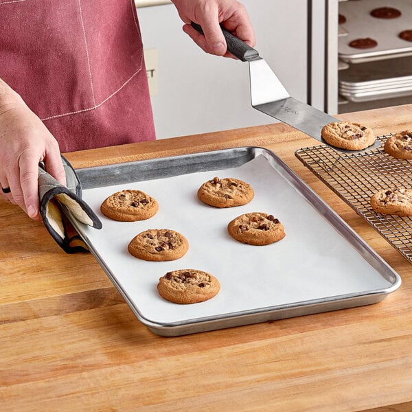 A person using a Baker's Lane parchment paper sheet to put cookies on a tray.