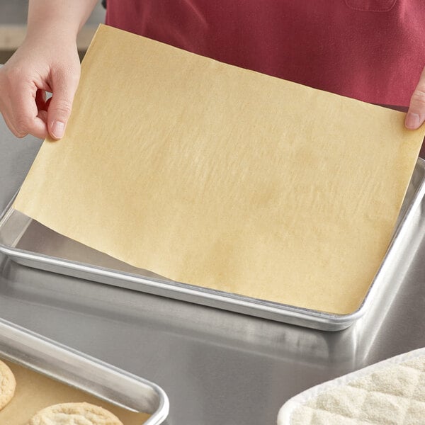 A person holding a Baker's Lane unbleached Quilon coated parchment paper sheet over a baking tray.