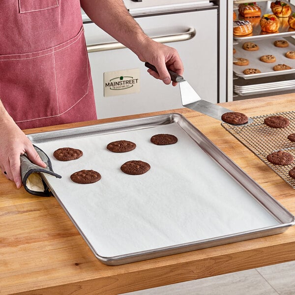 A hand using a metal spatula to put cookies on a Baker's Lane parchment paper-lined tray.