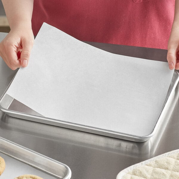 A person placing a Baker's Lane Quilon-coated parchment paper sheet on a baking tray.