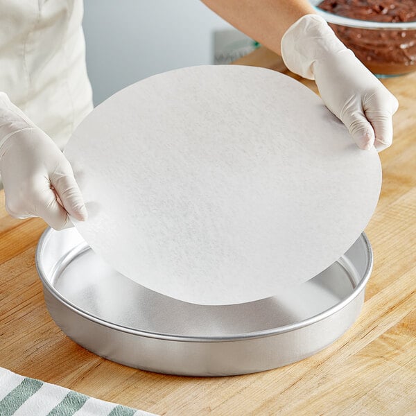 A person in gloves holds a Baker's Lane round dry wax parchment liner.