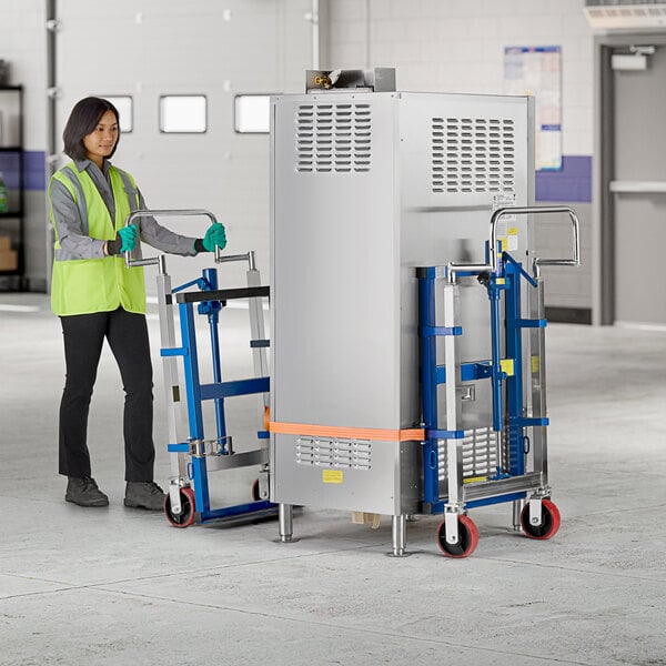 A woman wearing a yellow safety vest and gloves uses a Lavex hydraulic steel equipment mover to push a large grey box.