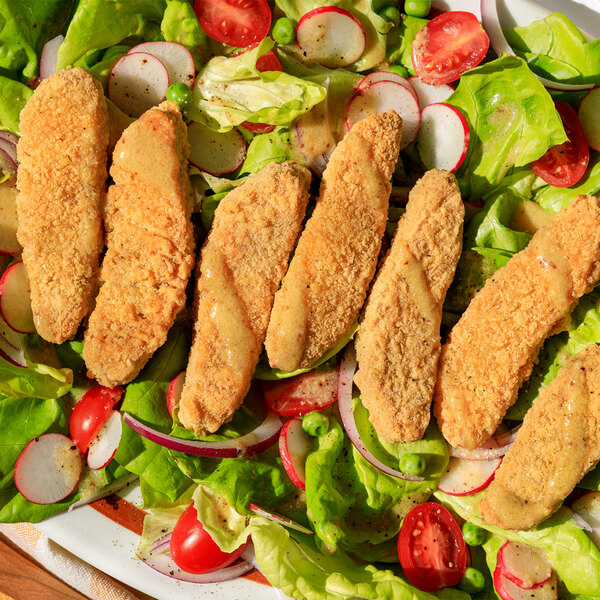 A plate of Jack & Annie's Vegan Plant-Based Chicken Tenders on a table with lettuce and radishes.