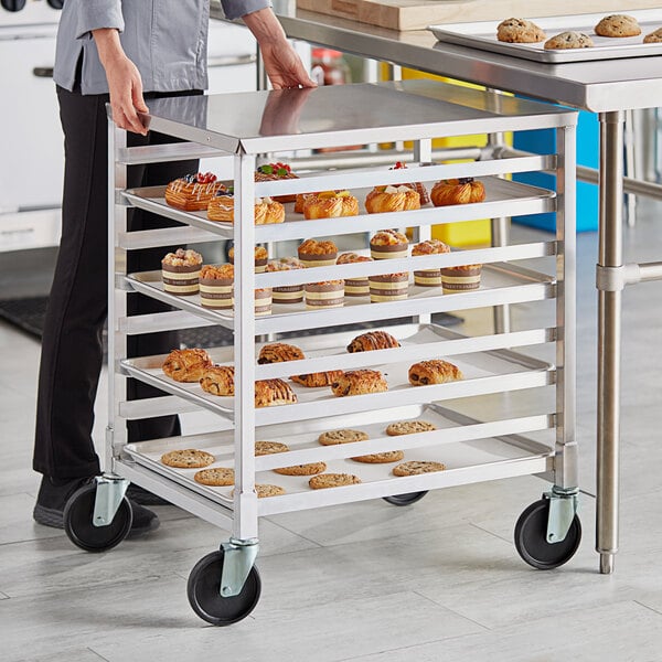 A woman standing next to a Regency undercounter sheet pan rack full of pastries.