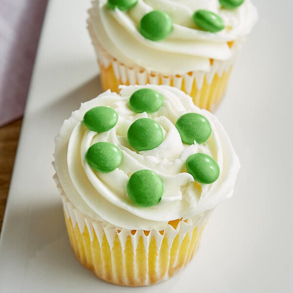 A cupcake with white frosting and green Milk Chocolate Gems on top.