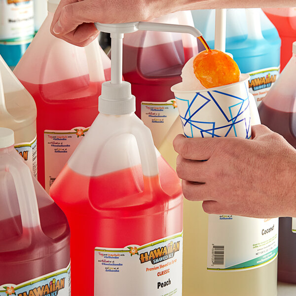 A person pouring Hawaiian Shaved Ice Peach Snow Cone Syrup from a plastic jug into a cup.