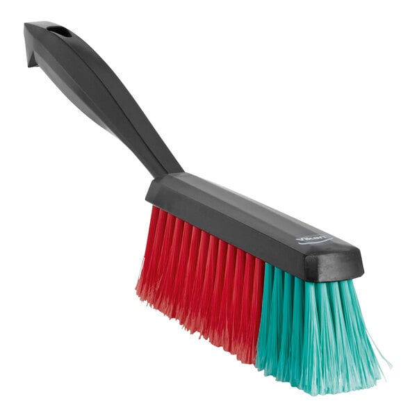 A close up of a Vikan Transport soft hand brush with black and green bristles with red and blue accents.