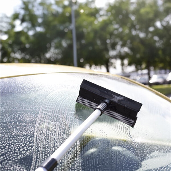 A windscreen scraper with a sponge and telescopic handle being used to clean a car windshield.