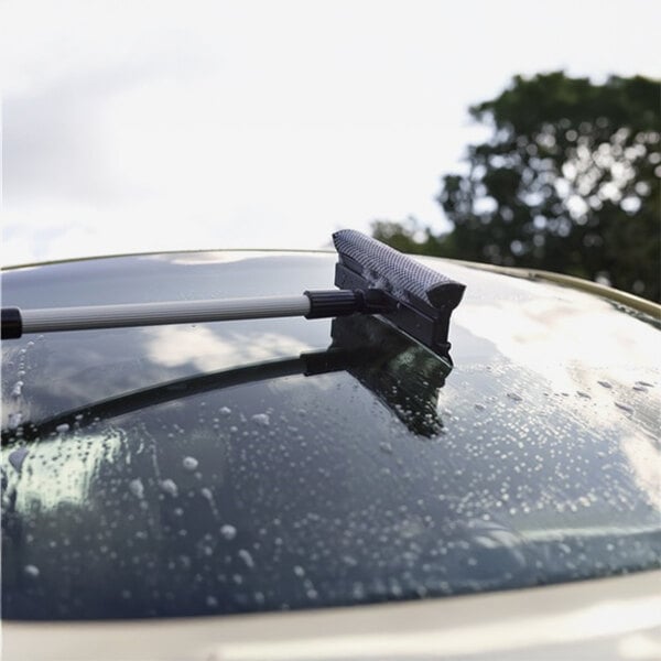 A windscreen scraper with a sponge and telescopic handle being used to clean a car windshield.