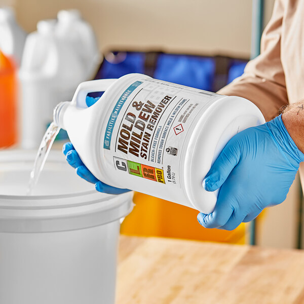 A person in blue gloves pouring CLR Mold & Mildew Stain Remover into a bucket.