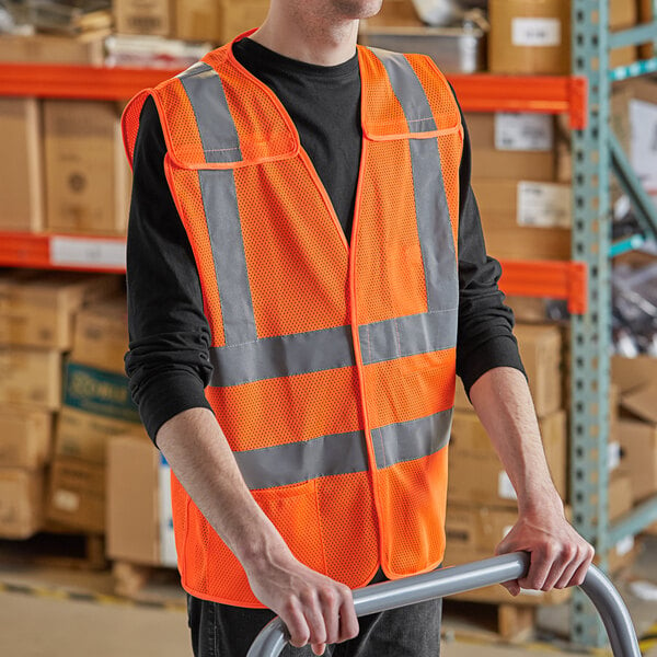 A man wearing a Lavex orange high visibility safety vest holding a handrail in a warehouse.