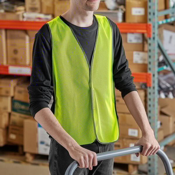 A man wearing a lime green high visibility safety vest pushing a hand truck.