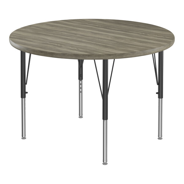 A Correll round activity table with black metal legs and a gray driftwood top with black edging.