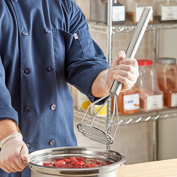 A person using a Fourt&#233; stainless steel potato masher on a bowl of red food.