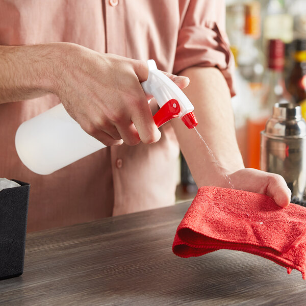 A person spraying a table with a red Lavex spray bottle using a red cloth.