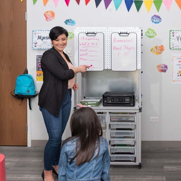 A woman standing next to a Luxor white steel teacher dry erase easel.