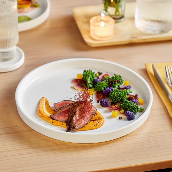 A Acopa Lore white porcelain plate with steak and vegetables on it.