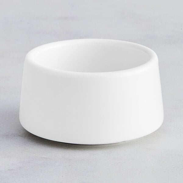 An Acopa Lore bright white porcelain sauce cup on a white surface.