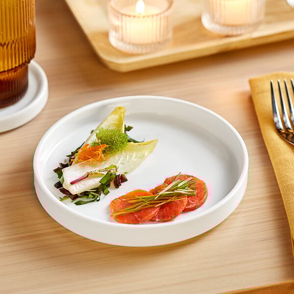 A plate of food on a wood table with an Acopa Lore bright white raised rim porcelain plate.