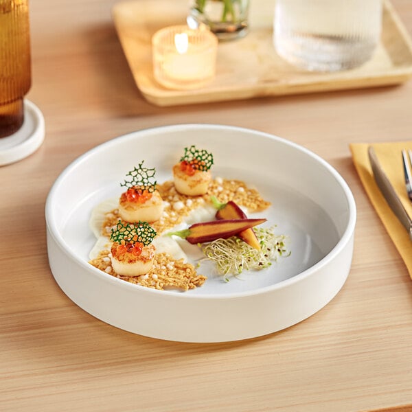 A white Acopa Lore porcelain deep plate with food on it on a table.