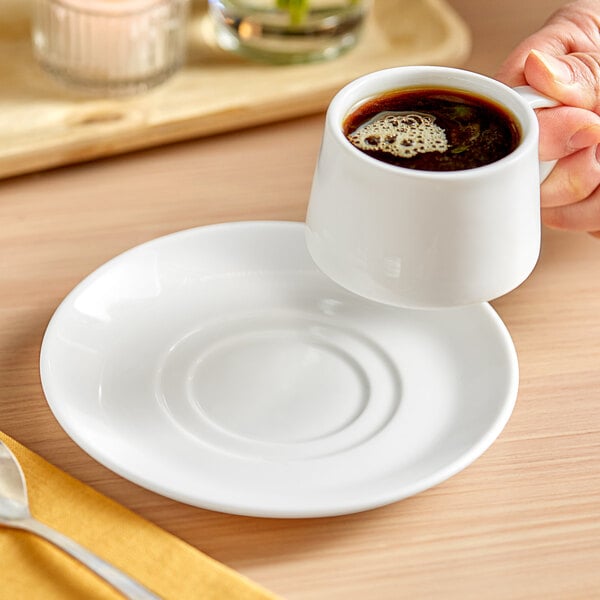 A person holding a white mug on a white Acopa Lore porcelain saucer.