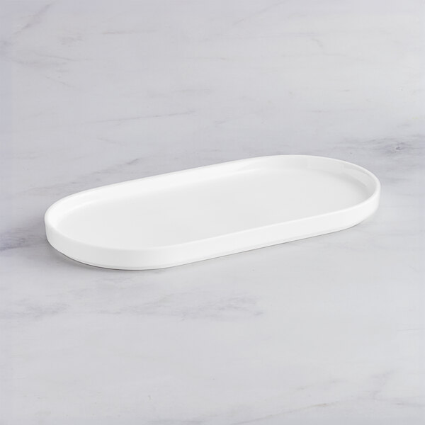 An Acopa Lore bright white porcelain rectangular platter with raised edges on a marble surface.