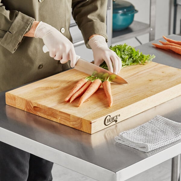 A person cutting carrots on a Choice wooden cutting board.