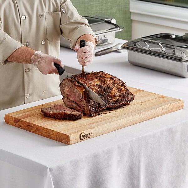 A chef cutting meat on a Choice wood cutting board.