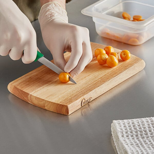 A person cutting a cherry tomato on a Choice wood cutting board.