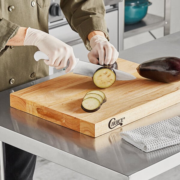 A person cutting eggplant on a Choice wood cutting board.