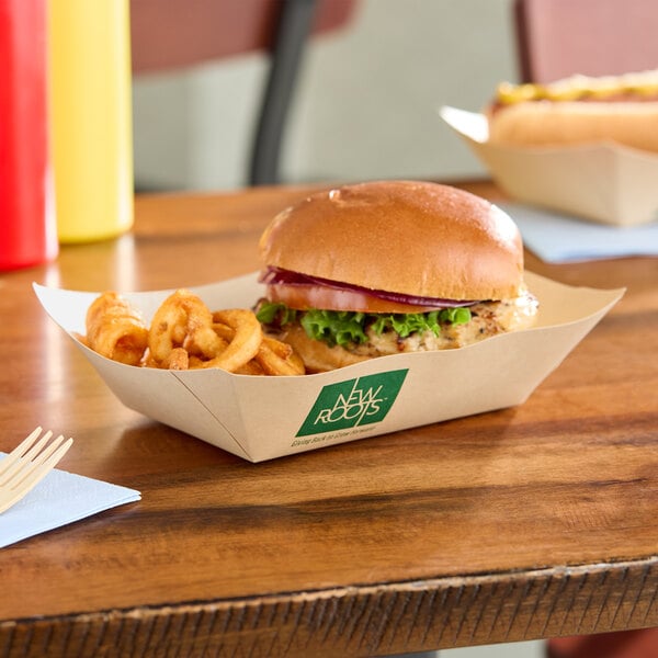 A rectangular compostable bamboo food tray containing a sandwich and curly fries on a wooden table.
