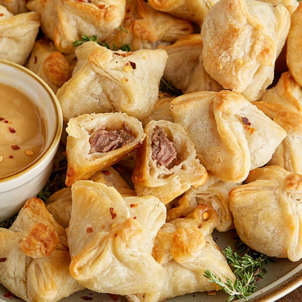 A plate of Cuisine Innovations Beef Wellington En Croute with a bowl of brown dipping sauce.