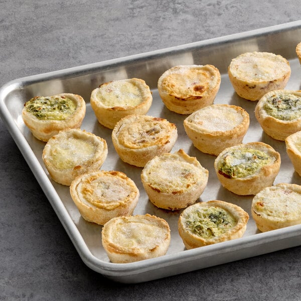 An assortment of mini quiches arranged on a metal baking tray.
