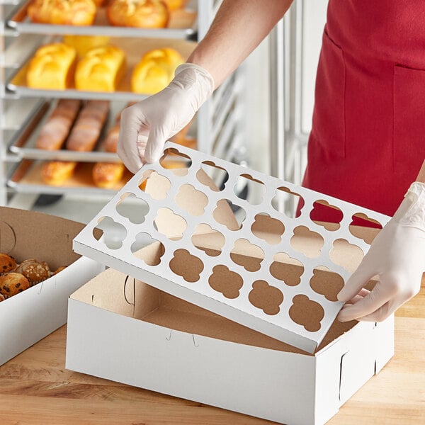 A person holding a white box with holes in it filled with mini cupcakes.