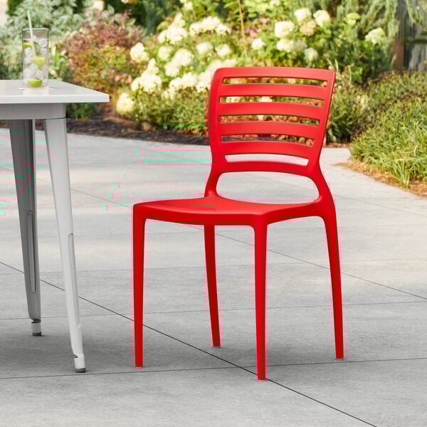 A red Lancaster Table & Seating Sol Buoy resin chair on a patio next to a table.