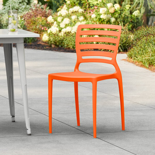 A Lancaster Table & Seating orange resin chair on a patio.