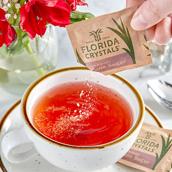 A hand holding a Florida Crystals Turbinado Cane Sugar packet over a cup of tea.