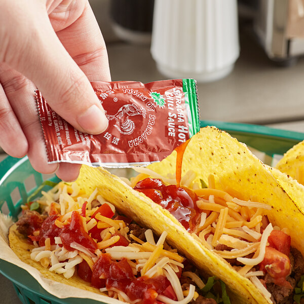 A person holding a red packet of Huy Fong Sriracha sauce.