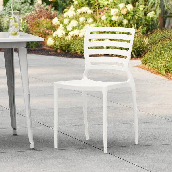 A Lancaster Table & Seating Sol Cloud White Resin side chair on a patio.