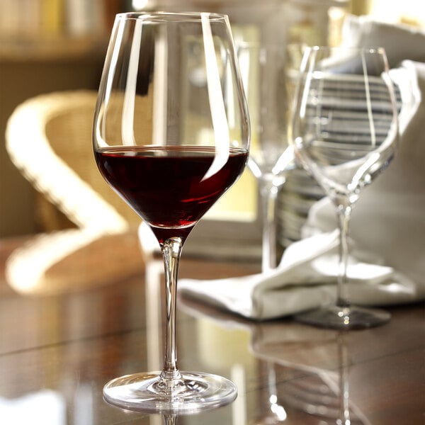 A Stolzle Bordeaux wine glass filled with red wine on a table.