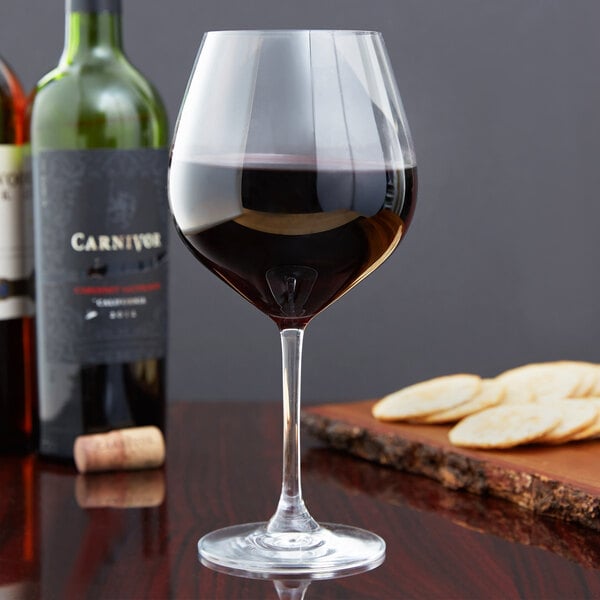 A Stolzle Grand Cuvée burgundy wine glass filled with red wine on a table in a winery cellar.